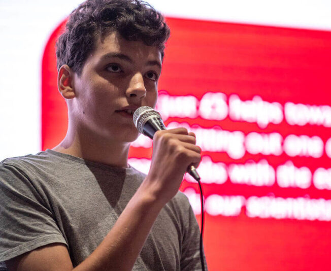 Male SBC student with a presentation back drop, reading his presentation into a microphone