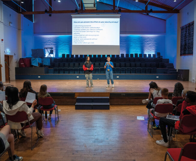 Two student stood on a stage giving their Art & Design Time to Shine Presentation